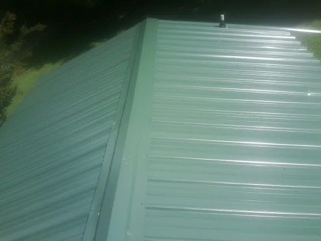 New green metal panels meeting at the ridge of a roof — Flat Roof Repair work by our crew in Euclid